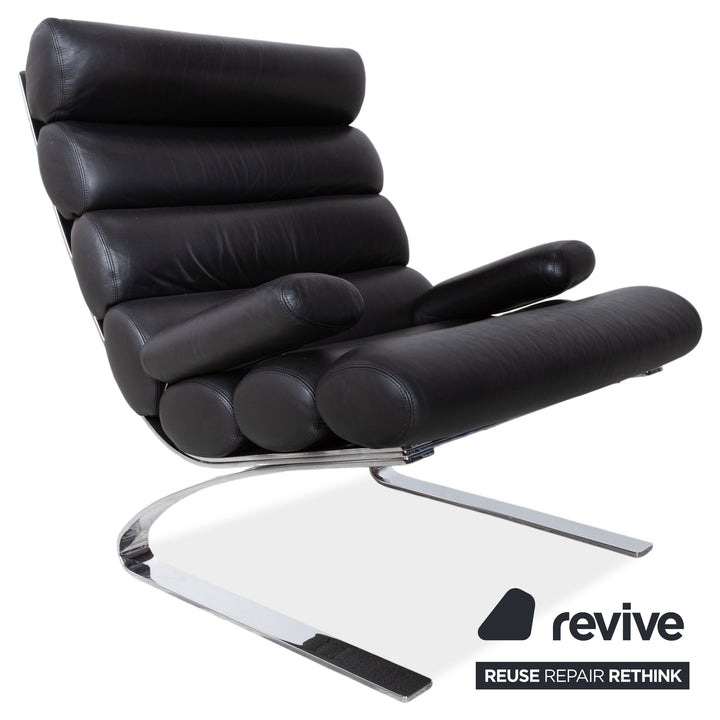 Fauteuil Cor Sinus en cuir chromé noir avec repose-pieds et bras articulés.