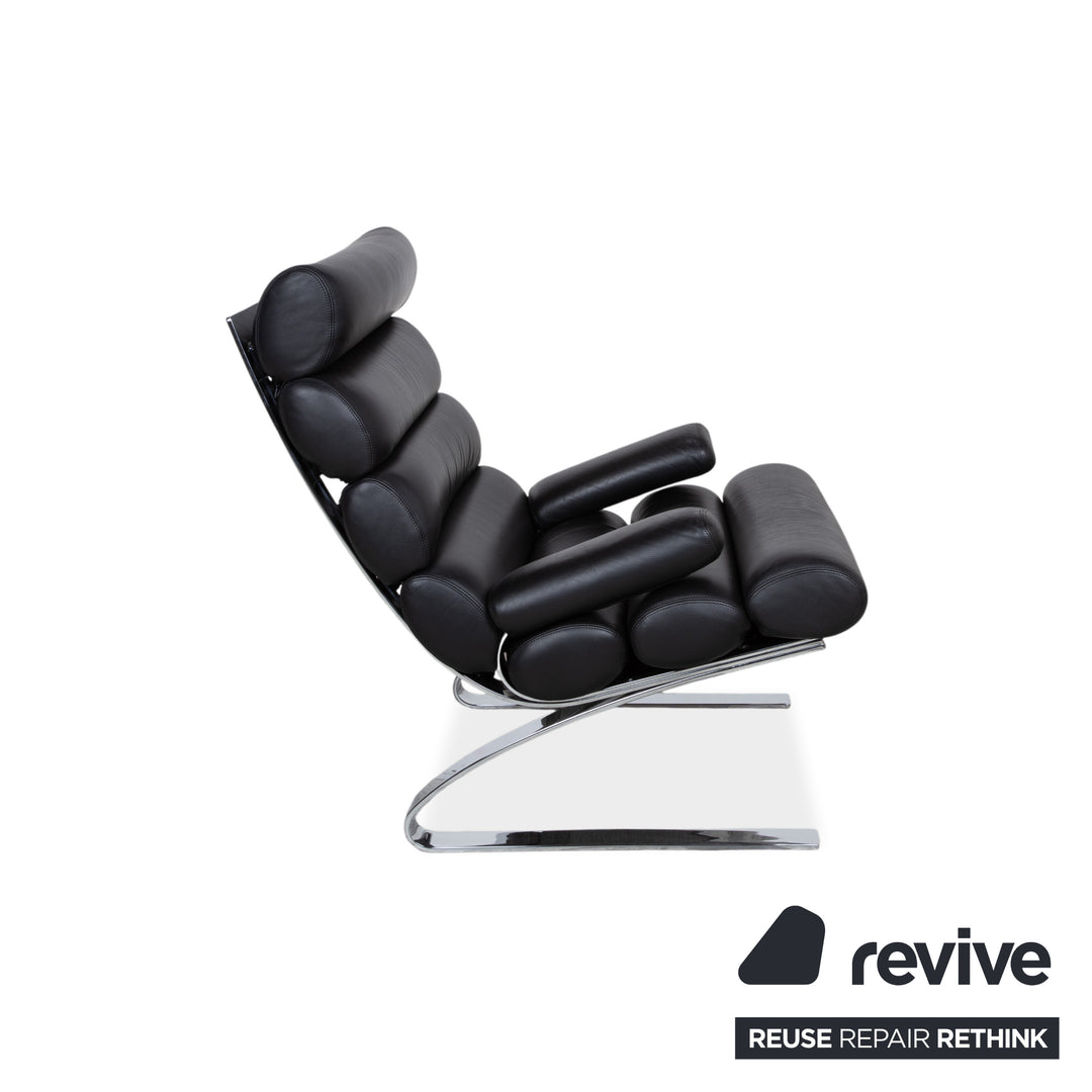 Fauteuil Cor Sinus en cuir chromé noir avec repose-pieds et bras articulés.