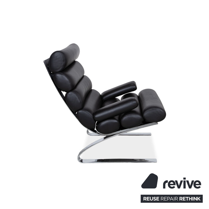 Fauteuil Cor Sinus en cuir chromé noir avec repose-pieds et bras articulés.
