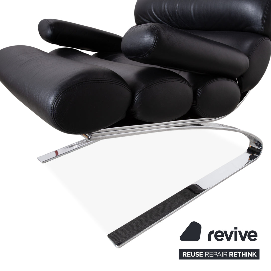 Fauteuil Cor Sinus en cuir chromé noir avec repose-pieds et bras articulés.