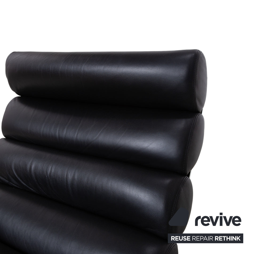 Fauteuil Cor Sinus en cuir chromé noir avec repose-pieds et bras articulés.