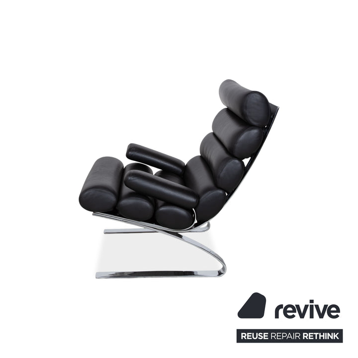 Fauteuil Cor Sinus en cuir chromé noir avec repose-pieds et bras articulés.