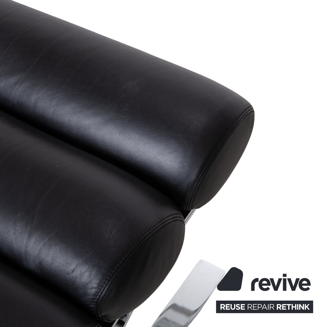 Fauteuil Cor Sinus en cuir chromé noir avec repose-pieds et bras articulés.