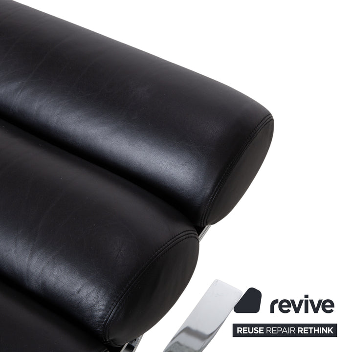 Fauteuil Cor Sinus en cuir chromé noir avec repose-pieds et bras articulés.