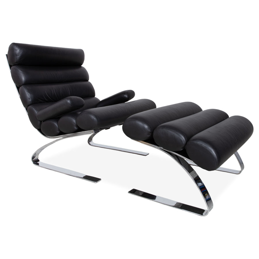 Fauteuil Cor Sinus en cuir chromé noir avec repose-pieds et bras articulés.